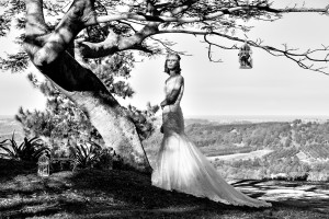 Black & white photo of a bride standing under a large flame tree in her wedding gown designed by Gold Coast Bridal Lounge