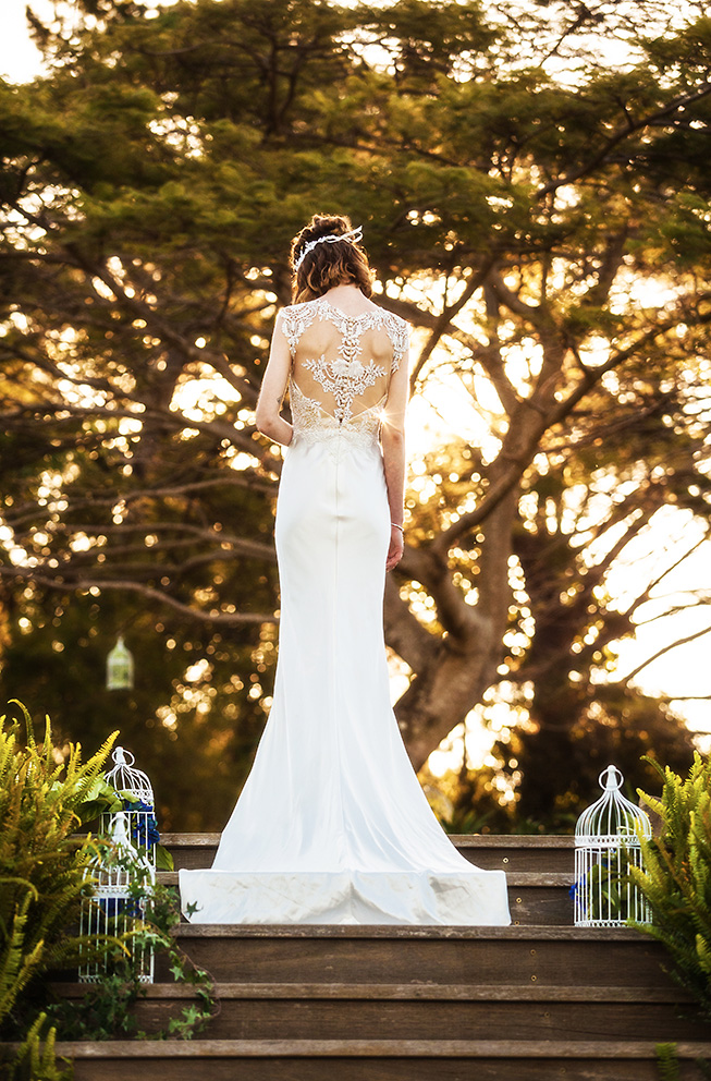 Photo from behind of a bride standing in front of trees and a sunset in her wedding gown designed by Gold Coast Bridal Lounge, Australia