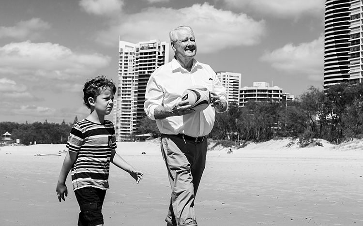 An image of a boy walking on a beach with his grandfather holding a rugby ball.